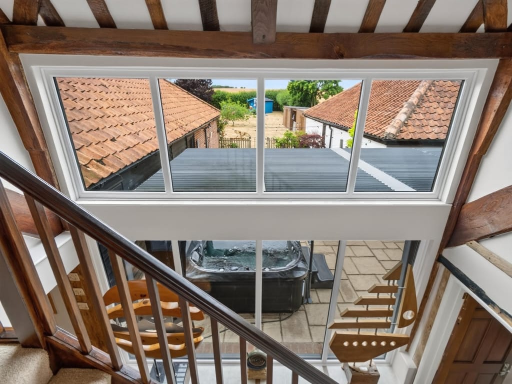 Staircase landing with oak beams, large picture window overlooking courtyard hot tub and barn rooftops, The Tithe Barn, Sisland, Norfolk