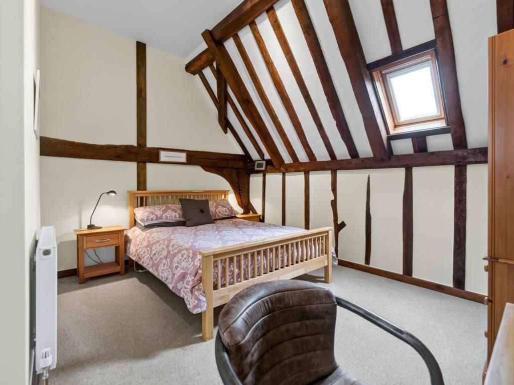Bedroom with exposed timber frame, sloping beamed ceiling, Velux window, and double bed at The Tithe Barn, Sisland, Norfolk
