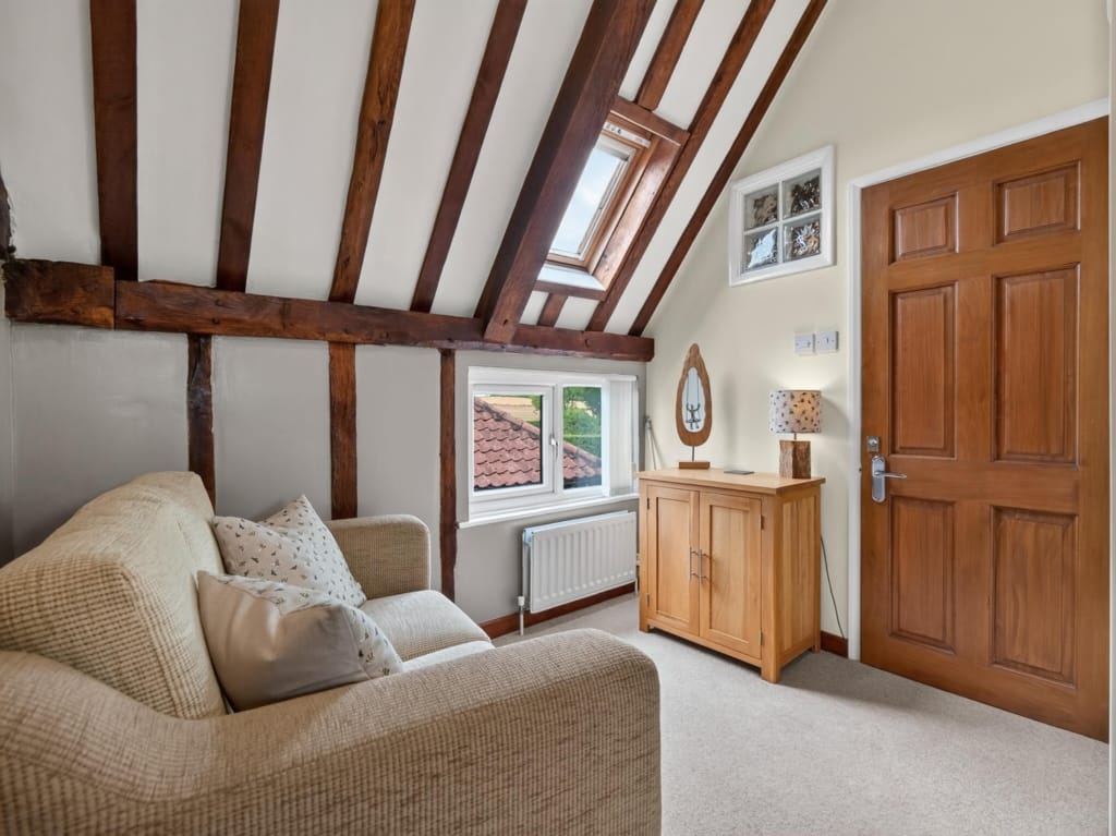 Sitting area with exposed timber roof beams, Velux skylight, and oak sideboard in one of the holiday barns at Sisland, Norfolk