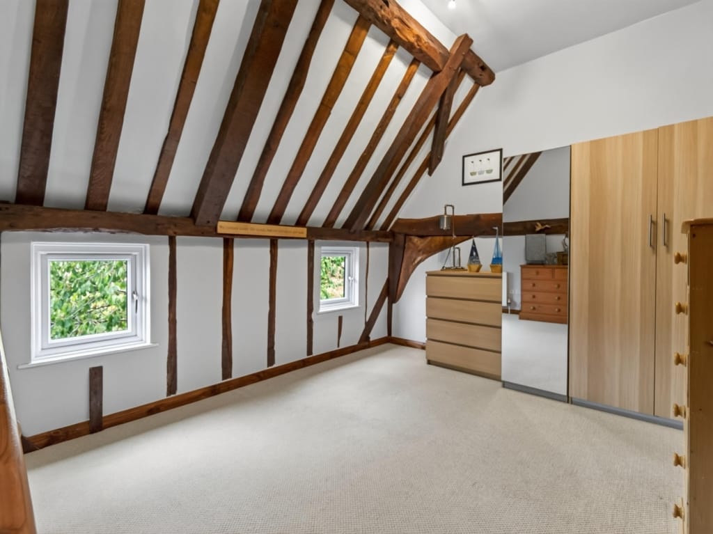Bedroom with exposed timber roof trusses, fitted wardrobes, and two casement windows at The Tithe Barn, Sisland, Norfolk