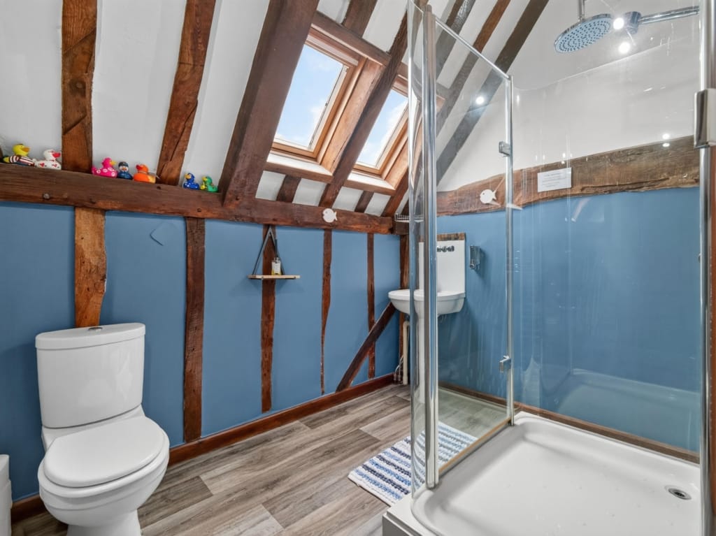 Family bathroom with exposed timber beams, skylight windows, glass shower enclosure and blue walls at The Tithe Barn, Sisland, Norfolk