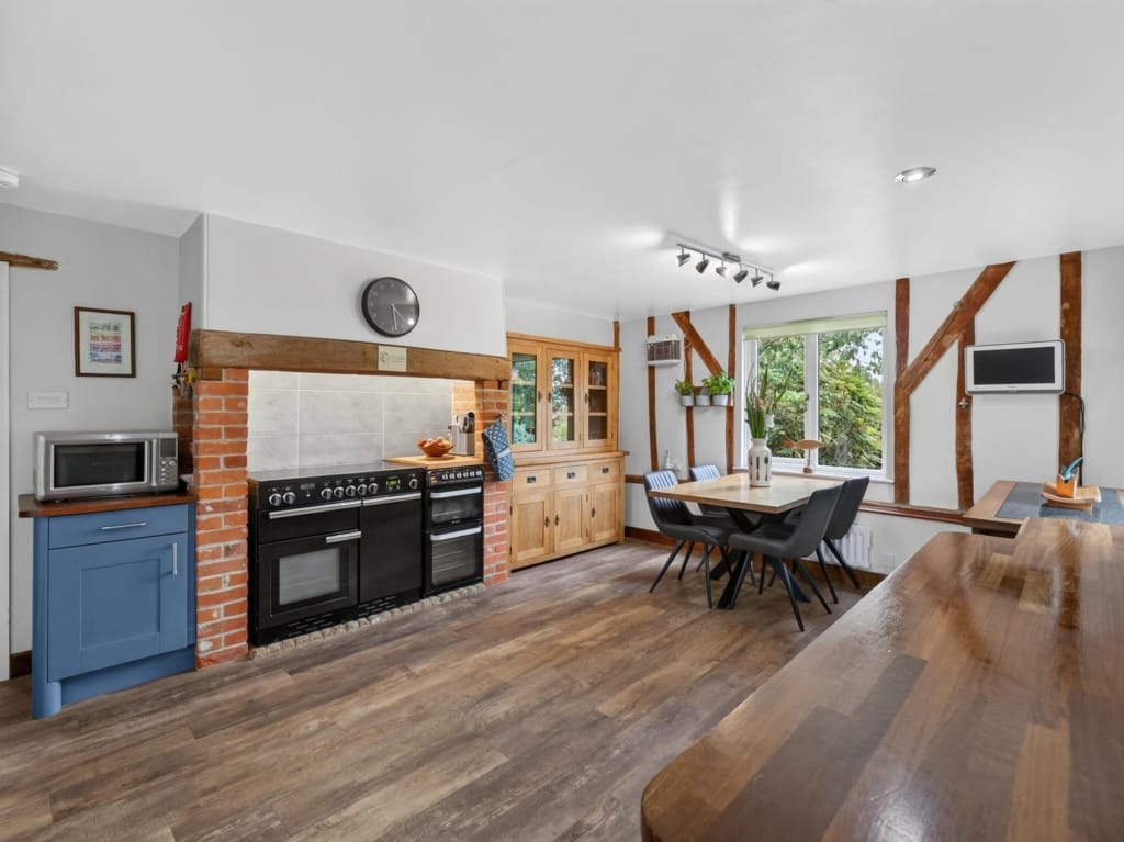 Kitchen and breakfast room with range cooker in brick recess, exposed timber frame, and dining table, The Tithe Barn, Sisland, Norfolk
