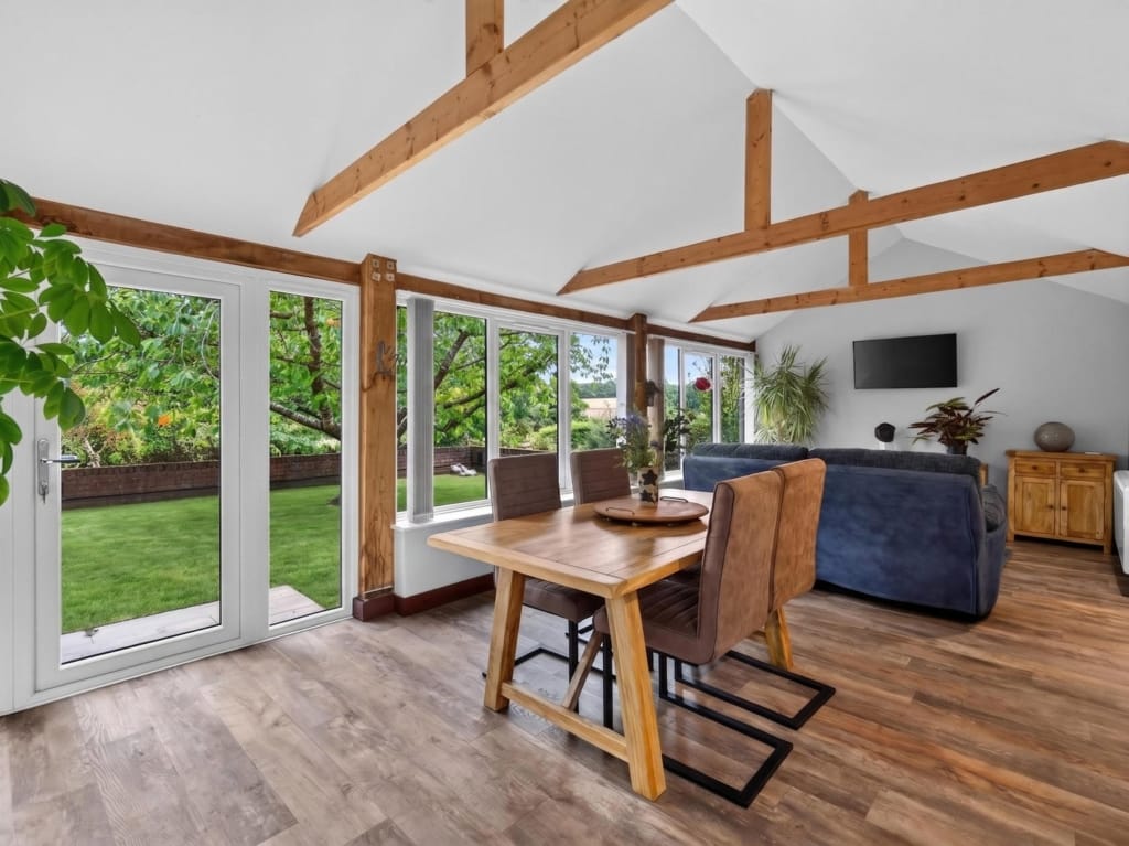 Open-plan living area with vaulted timber beams, oak dining table, and French doors opening to lawned garden, The Tithe Barn, Sisland, Norfolk