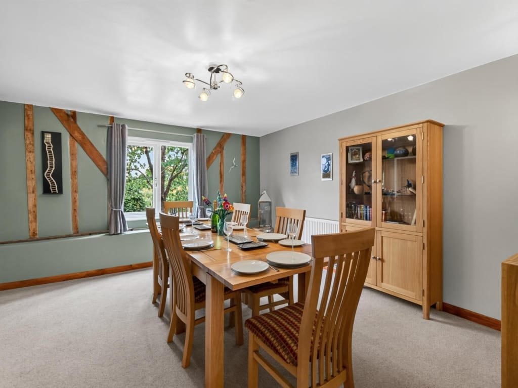Dining room with exposed timber frame, laid oak table, and garden-facing window at The Tithe Barn, Sisland, Norfolk