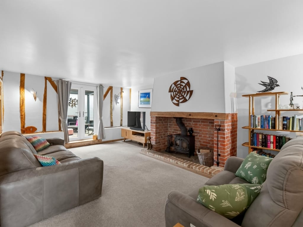 Sitting room with exposed timber frame, brick fireplace with log burner, and French doors, The Tithe Barn, Sisland, Norfolk