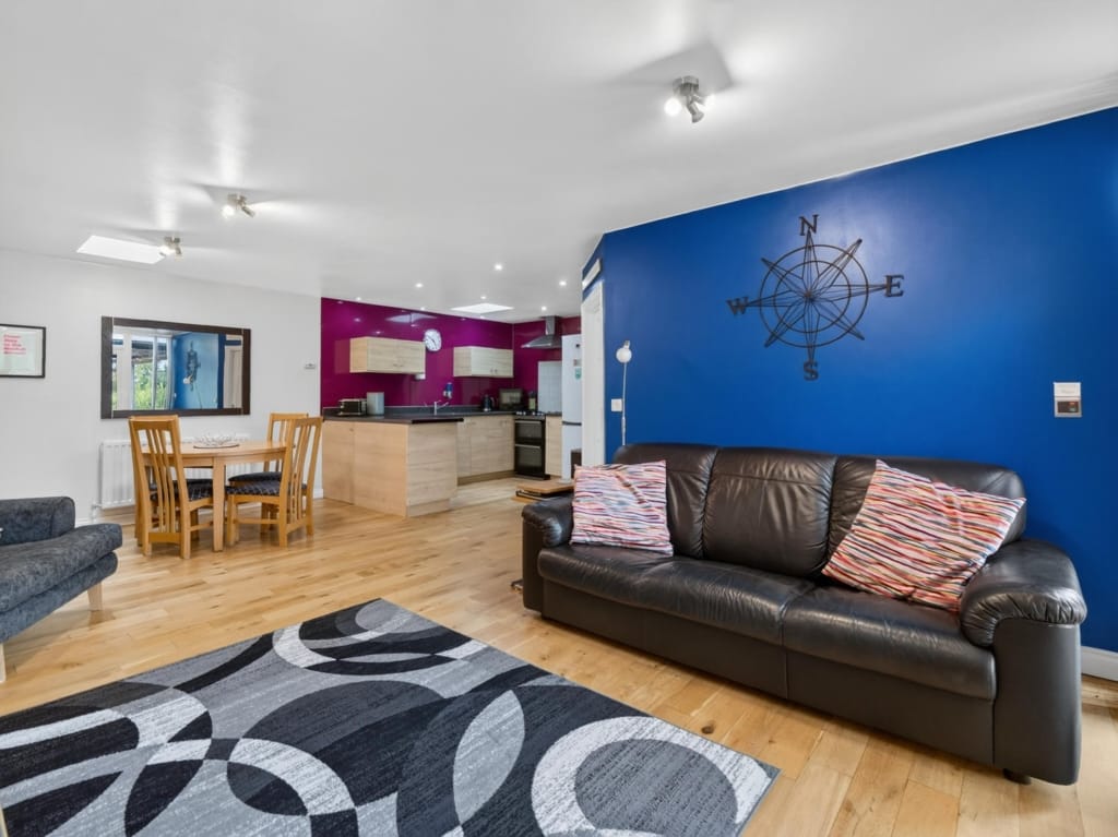 Open-plan living area in Owl Barn, Sisland, with leather sofa, blue feature wall, and kitchen beyond