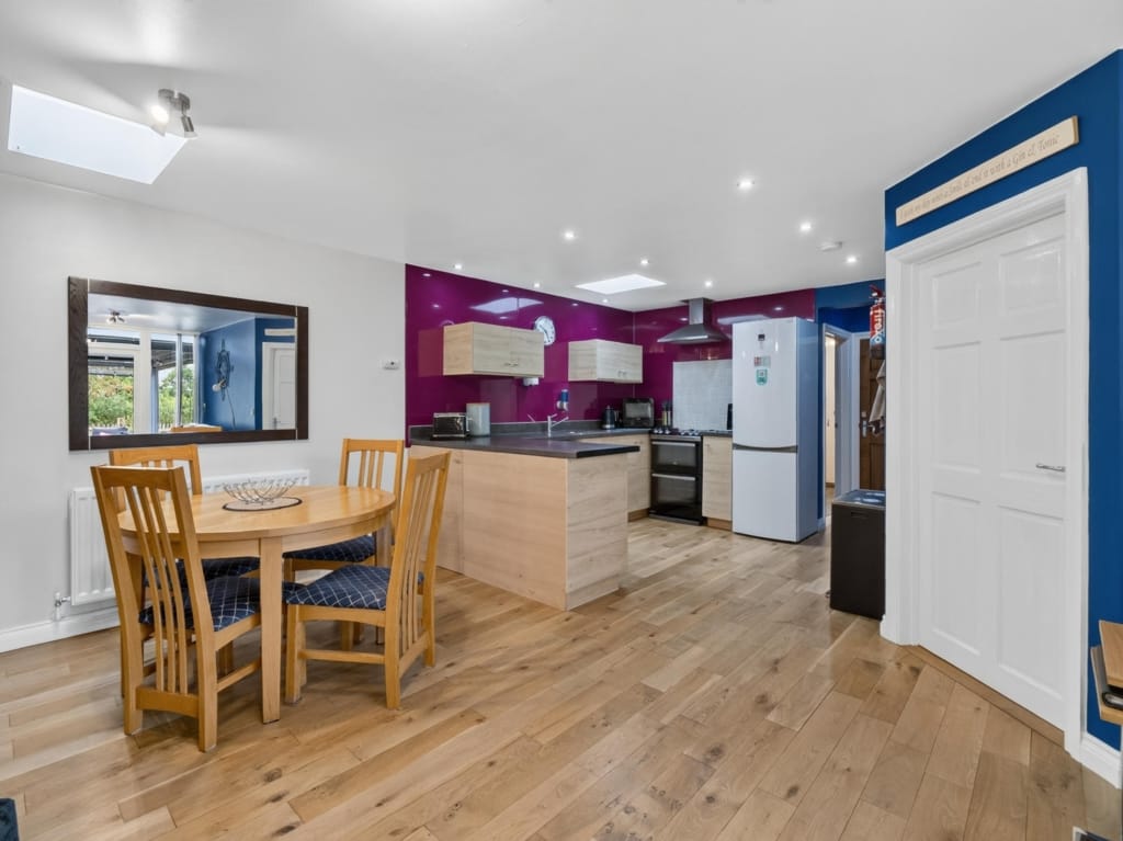 Kitchen and breakfast room with oak dining table, magenta splashback, island unit, and pale wood flooring at The Tithe Barn, Sisland, Norfolk