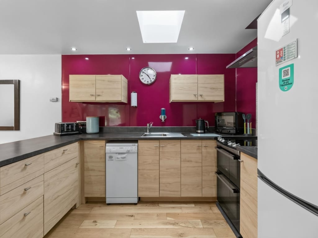 Holiday barn kitchen with magenta splashback, oak-effect units, skylight, and integrated appliances, Sisland Norfolk