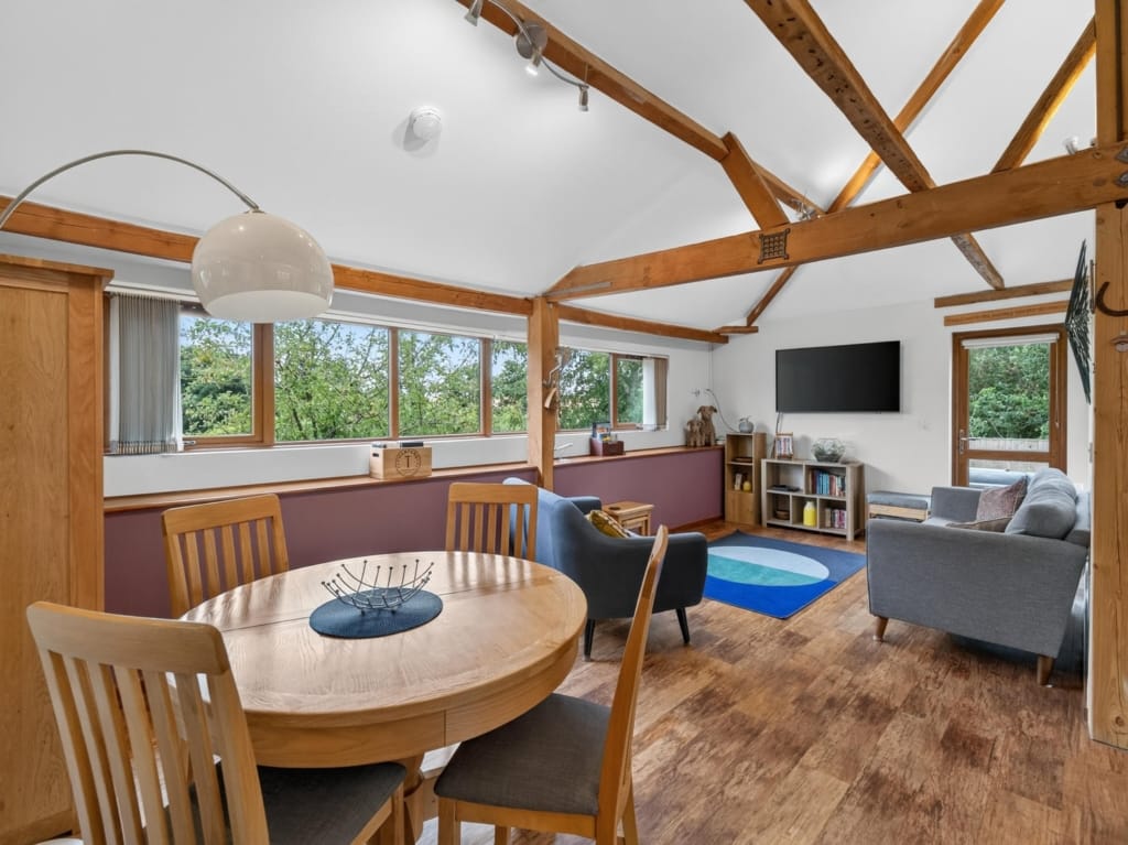 Open-plan living and dining area in a holiday barn with vaulted timber trusses, round oak table, and garden views, Sisland, Norfolk