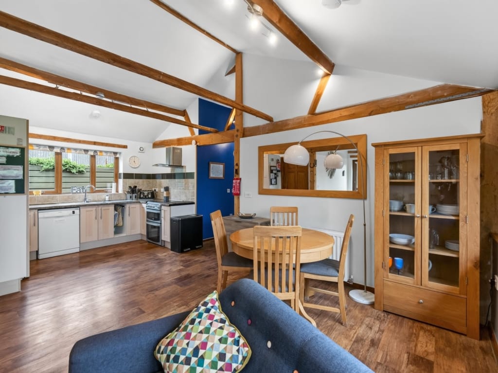 Open-plan living kitchen dining area in holiday barn with exposed timber beams, round oak table, and fitted kitchen, The Tithe Barn, Sisland, Norfolk