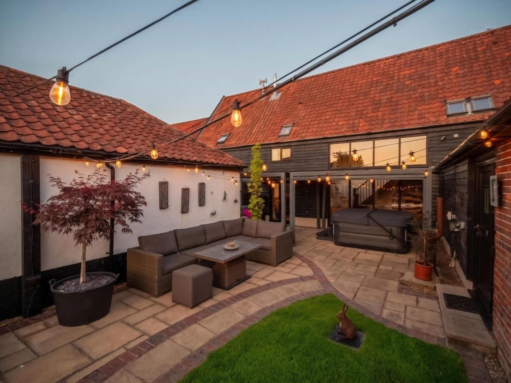 Courtyard garden at dusk with rattan seating, festoon lights, hot tub, and red pantile rooflines, The Tithe Barn, Sisland, Norfolk