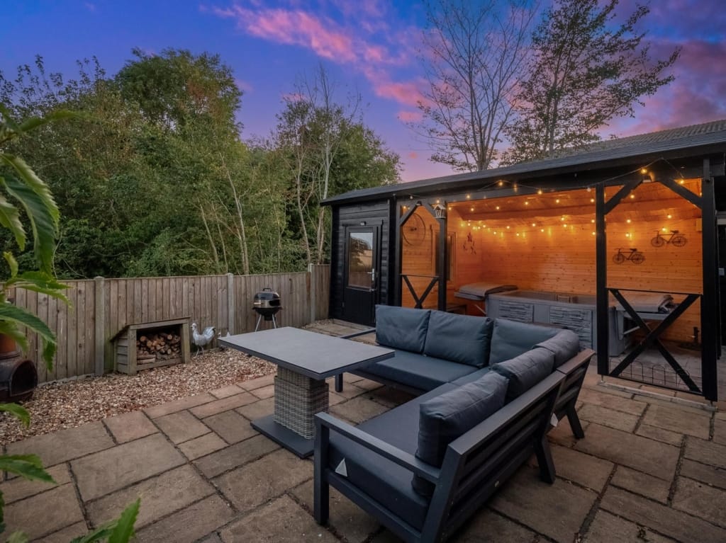 Outdoor patio at dusk with corner sofa, festoon-lit timber gazebo and hot tub, The Tithe Barn, Sisland, Norfolk