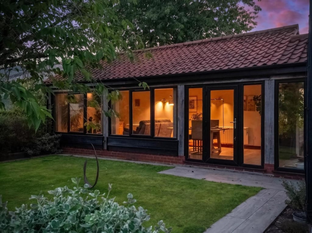 Holiday let barn exterior at dusk, lit glazed doors, pantile roof, lawn, Sisland Norfolk