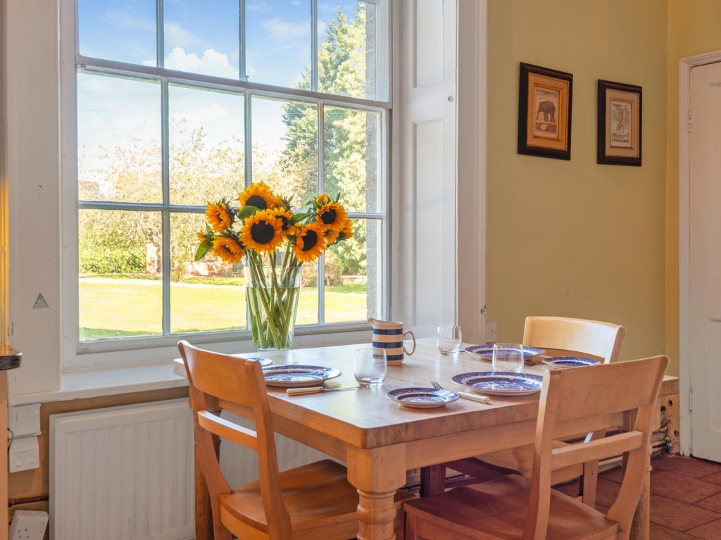 Breakfast table by a tall Georgian sash window in the kitchen at Loddon Hall, Norfolk