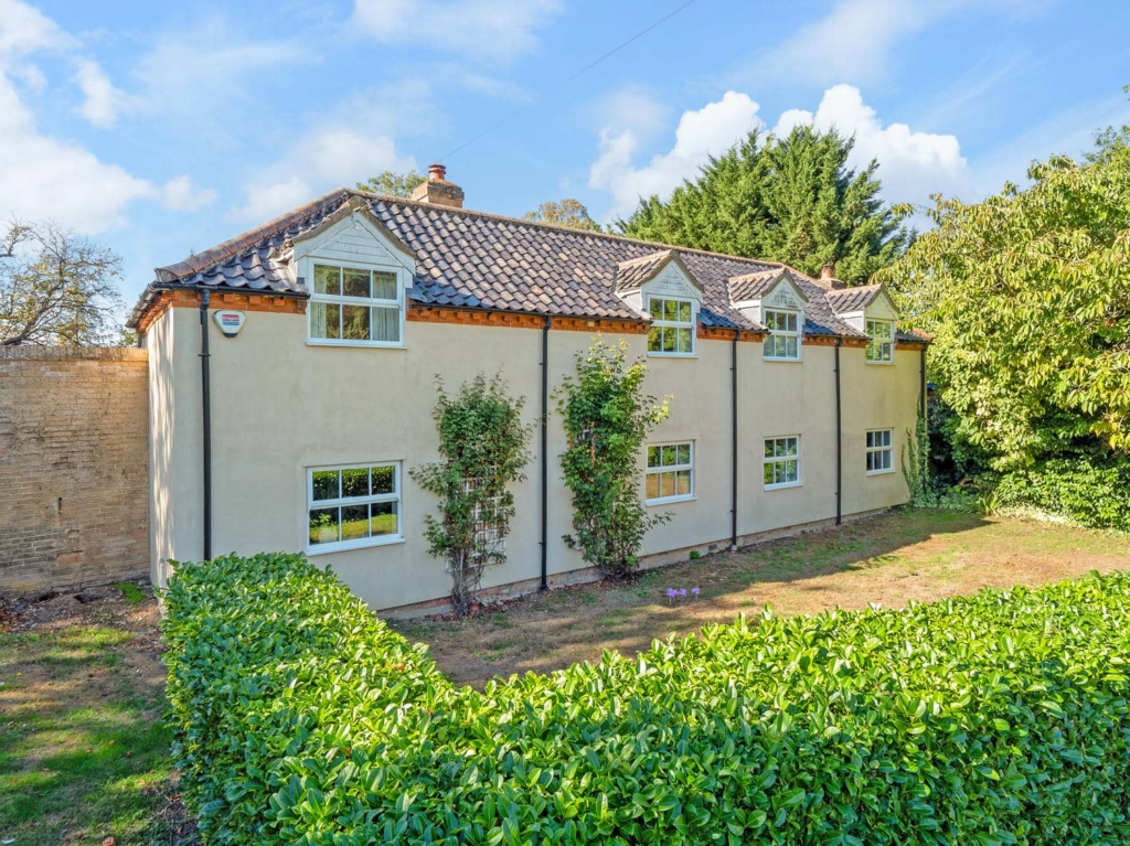 Front of Loddon Hall Cottage, a detached cream house with dormer windows and clipped hedge, Norfolk