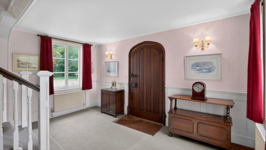 Entrance hall at The Priory Suffolk with arched oak front door, half-height panelling and staircase