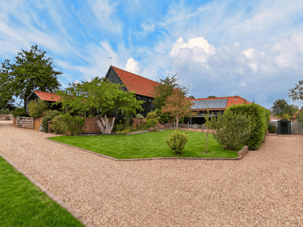 Exterior of The Tithe Barn Sisland showing black timber cladding, red pantile roofs, gravel driveway, and manicured front lawn